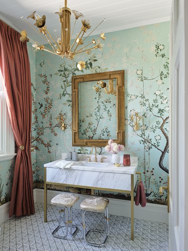 Hollywood regency bathroom with Chinoiserie wallpaper mural, floral Sputnik chandelier, coral curtains, and white marble vanity