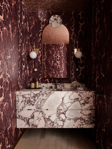 Modern Hollywood regency powder bathroom in burgundy and white with marble slab vanity, art deco sconces and burgundy marble print wallpaper