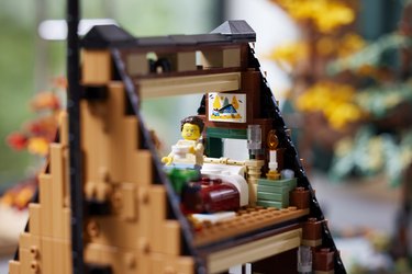 The lofted bedroom in the LEGO A-Frame cabin featuring a minifigure sipping coffee on a bed next to a green nightstand with a candlestick.