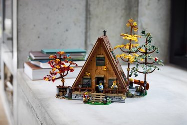 The LEGO A-Frame cabin complete with three fall trees and four minifigures on a gray wood counter.