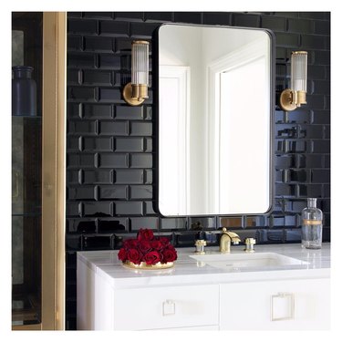 Modern Hollywood Regency bathroom with black tile wall, white vanity, fluted glass and brass sconces and brass accents
