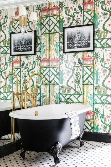 Hollywood regency bathroom with Chinoiserie bamboo pastel wallpaper, black clawfoot bathtub, brass hardware and black and white geometric tile floor