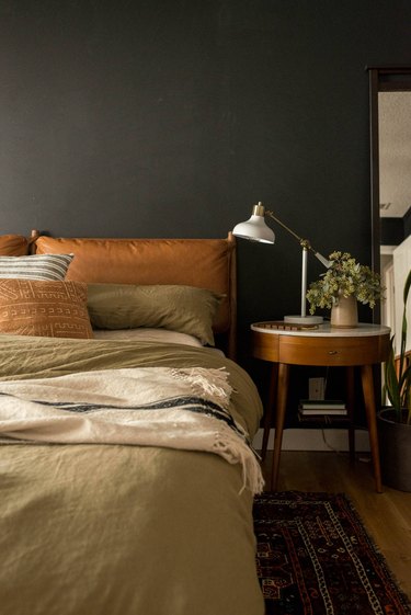 bedroom with black walls, leather headboard, and sage green and beige bedding