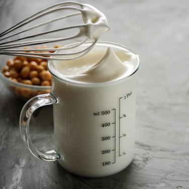 A measuring cup full of aquafaba with a wisk above.