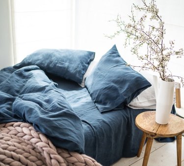 bed with blue linen sheets and small table with plant in white vase