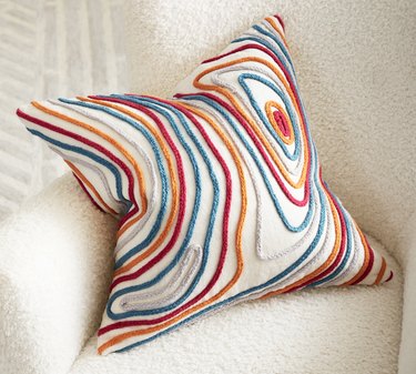 A throw pillow with red, orange and blue stitched pattern