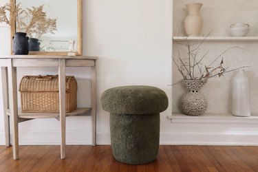 Green sherpa mushroom stool next to table with gold mirror and shelf with vases