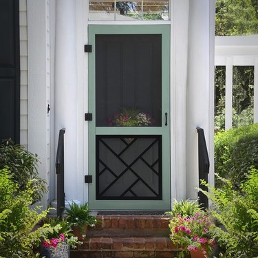 A green traditional screen door on a white house with a brick porch
