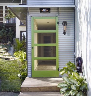 A lime green mid-century style screen door on a house with metal siding