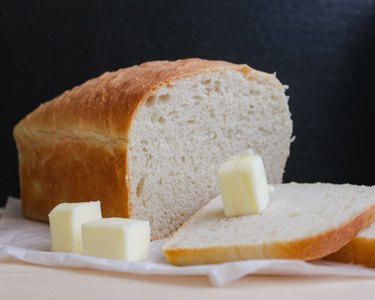 Half a loaf of white bread with three cubes of butter in front of a black background.