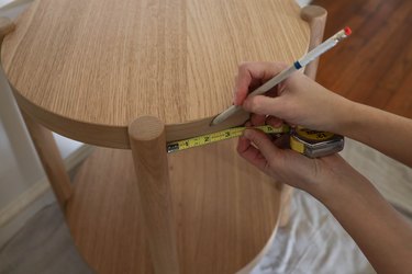 Marking spacing on top perimeter of table with pencil and tape measure