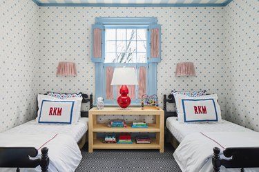 Children's bedroom with twin beds, wallpaper with blue stars, painted striped ceiling and blue shutters with red and white fabric inserts