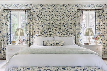 Maximalist granny chic bedroom with cornflower blue floral print wallpaper, curtains, and upholstered bed.