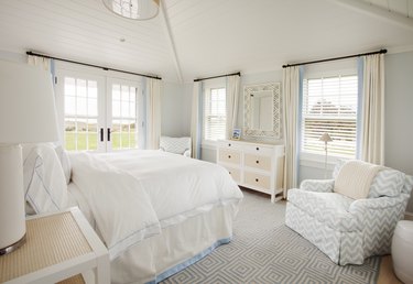 White and blue bedroom with vaulted ceiling, large windows and French doors