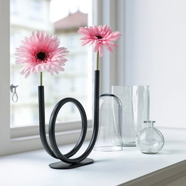 black loopy vase with pink flowers near glasses and vases