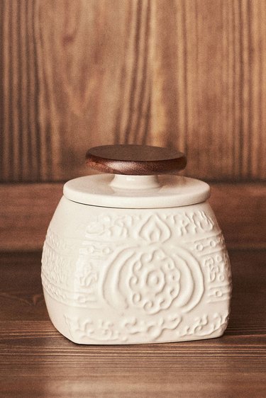 A white butter keeper with a dark wooden top rests on a wooden surface,
