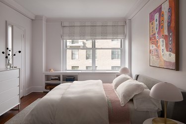 White, pink and gray bedroom with large art print above the bed and roman shade with gray stripes on the window