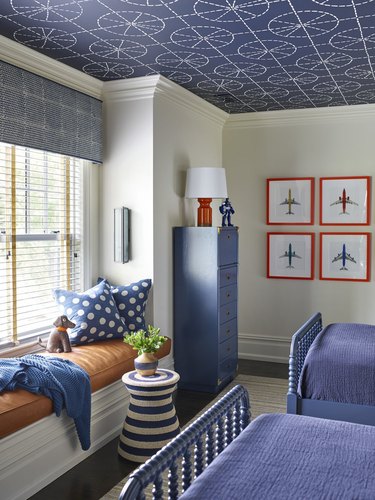 Kids' bedroom with blue wallpapered ceiling, blue and orange accents and a blue patterned valance on the window