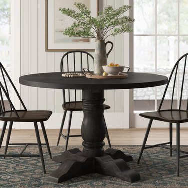 Round farmhouse dining table and chairs, vase, flowers, rug.