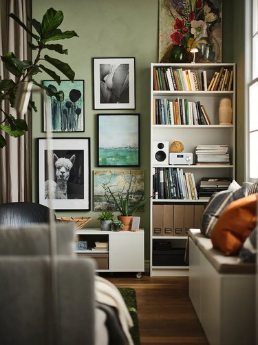 A white bookshelf surrounded by a gallery wall or art and plants.