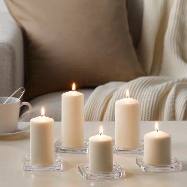 Five beige candles of different styles on glass plates on a cream-colored coffee table.