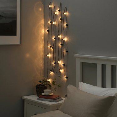 String lights hanging vertically in a darkened room next to a beige and white bed.