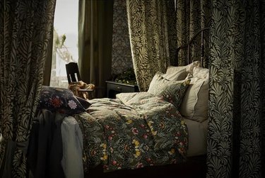 A dark floral bed with matching curtains next to a window.