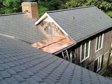 A large farmhouse-style house with a gray synthetic roof and a brick chimney