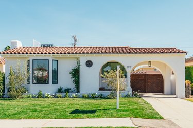 Spanish house with a clay roof tile, front lawn, arch, wood gate, driveway.