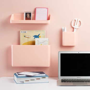 desk area with pink wall pockets on pink wall and laptop and book on desk