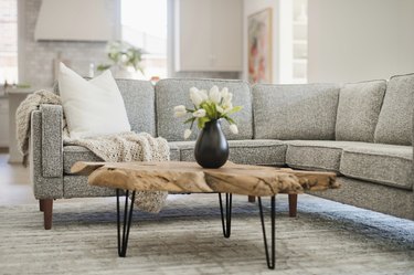 A gray sectional with a rustic wooden coffee table with a black vase on top