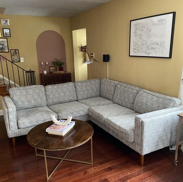 A gray sectional in a yellow living room; a brown round coffee table with books