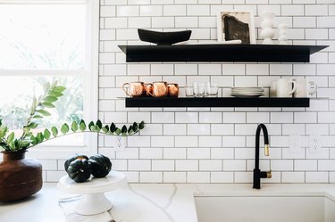 white kitchen tile wall near faucet with two black floating shelves