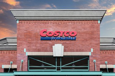 A photo of a Costco warehouse with a red Costco logo and blue sky in the background.