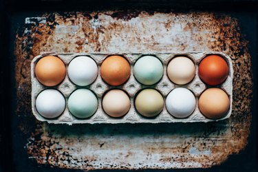 Pastel-colored eggs in a egg tray on a rusted surface.