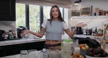 Hailey Bieber in her kitchen with navy blue cabinetry and marble countertops.