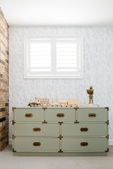 sage green dresser next to brown brick wall