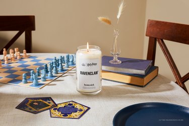 Homesick's Ravenclaw candle on a white dining table with a blue and white chess board and a Ravenclaw chocolate frog card.