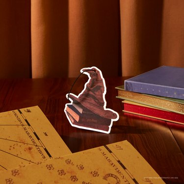 A Sorting Hat Air Freshener on a wood table next to a Marauder's Map.