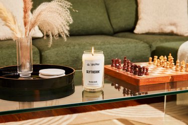 Homesick's Slytherin candle on a glass coffee table with a wood chess set and pampas grass in a clear vase.