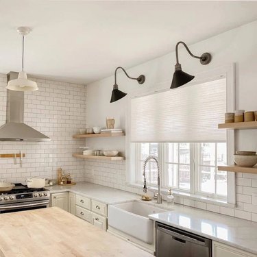 Cellular shades in a kitchen with open shelving, white subway tile, and two black sconces above the window