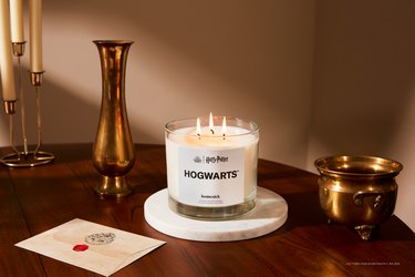 Homesick's Hogwarts Triwick canle on a marble trivet on a dark wood table next to a Hogwarts acceptance letter.