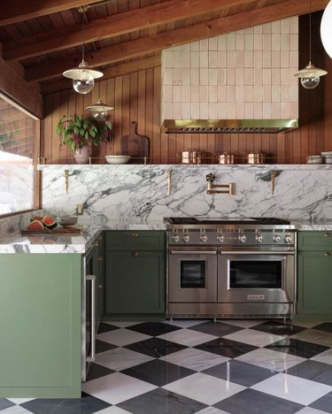 A green, gray, and dark wood kitchen with veined marble countertop and backsplash and checkerboard tile floor.