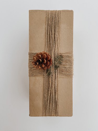 Add an evergreen sprig and pinecone to create a festive centerpiece on your gift box.