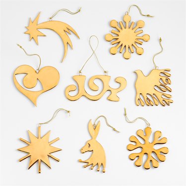 A gold ornament set featuring three suns, a comet, a typographic take on the word "joy," a whimsical donkey, a dove of peace, and Lucia Eames' signature Seeing with the Heart design.