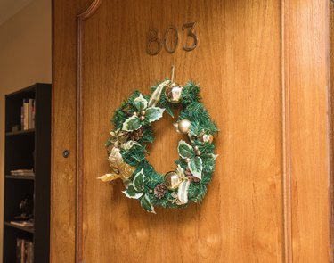 A green wreath with pinecones, small gold ornaments, and holly on an open wood front door.