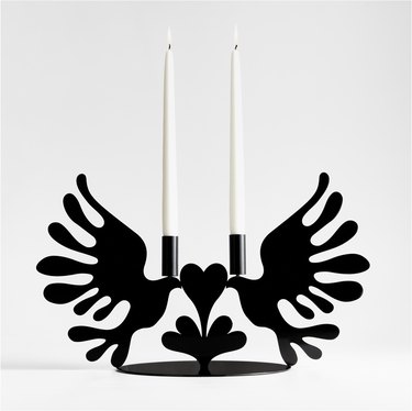 A black candelabra in the shape of two doves kissing a heart.