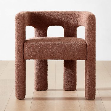 A dark brown bouclé dining chair with a low rounded back and four rounded bouclé legs.