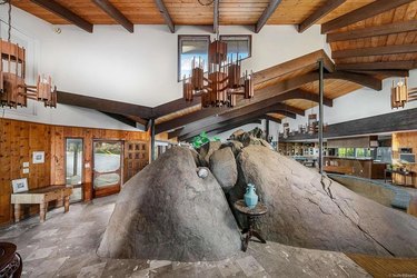 A living space with a brown chandelier and a large rock formation in the middle.