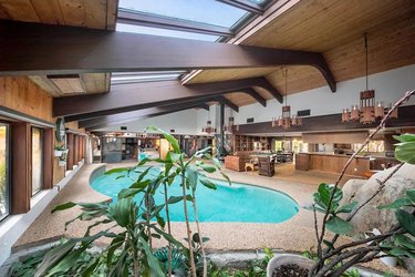 Another view of the swimming pool in the living room with high ceilings and the kitchen off the background.